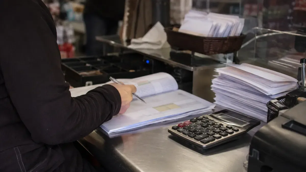 Planillas sin cifras, calculadora y sobres de cobros en un sector de caja sin marcas ni cifras, plano medio documental